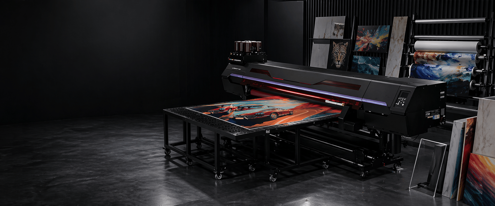 Large inkjet printer in a dark room with artwork displayed on screens and prints.